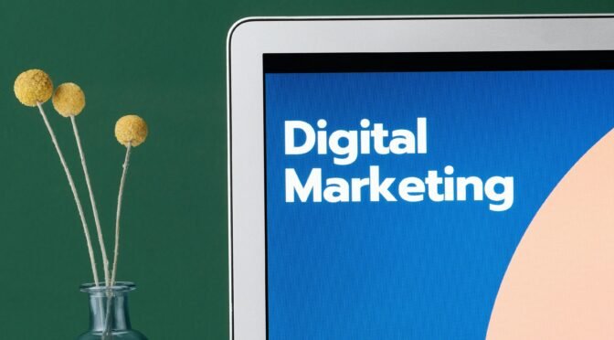 A laptop displaying 'Digital Marketing' with a minimalist floral decor in a glass vase.